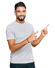 Young man with beard wearing casual grey tshirt smiling and looking at the camera pointing with two...