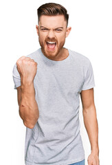 Young redhead man wearing casual grey t shirt angry and mad raising fist frustrated and furious while shouting with anger. rage and aggressive concept.