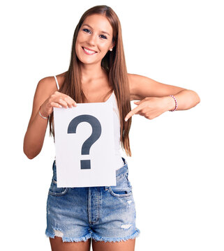 Young beautiful hispanic woman holding question mark smiling happy pointing with hand and finger