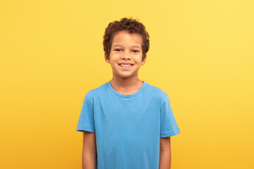 Portrait of smiling boy in blue shirt against yellow background - obrazy, fototapety, plakaty