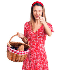 Young beautiful girl wearing picnic basket annoyed and frustrated shouting with anger, yelling crazy with anger and hand raised