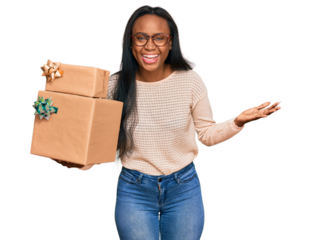 Young black woman holding gifts celebrating victory with happy smile and winner expression with raised hands