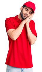 Young handsome man with beard wearing delivery uniform sleeping tired dreaming and posing with hands together while smiling with closed eyes.