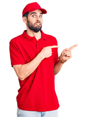 Young handsome man with beard wearing delivery uniform pointing aside worried and nervous with both hands, concerned and surprised expression