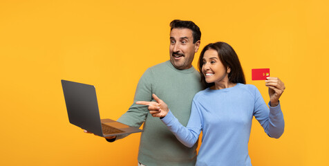 A man and woman in casual clothing excitedly make an online purchase, pointing at a laptop