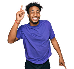 Young african american man with beard wearing casual purple t shirt pointing finger up with successful idea. exited and happy. number one.