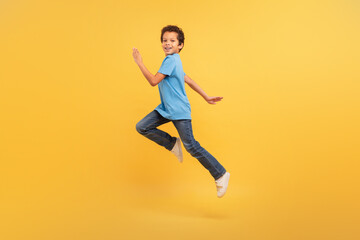 Fototapeta na wymiar Black boy in mid-run on bright yellow background