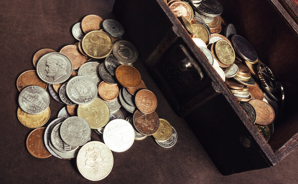 Photo of a wooden treasure box or chest filled with coins on table surface.
