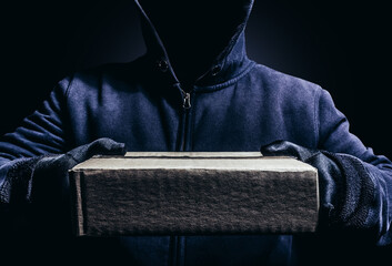 Photo of scary shaded hooded man giving a cardboard box parcel on dark background.