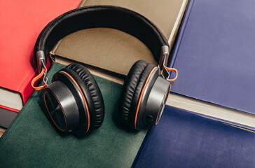 Photo of modern bluetooth headphones laying on various colored books, audio books library concept.