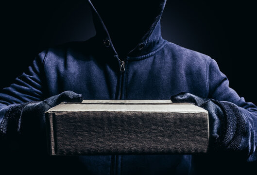 Photo of scary shaded hooded man giving a cardboard box parcel on dark background.