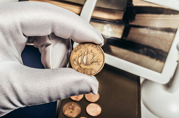 Photo of a person's male hand in white gloves holding a 1940 half penny british coin on stack of...