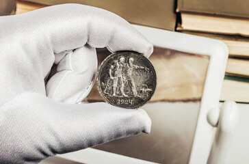 Photo of a person's male hand in white gloves holding a soviet silver 1924 ruble coin on stack of...