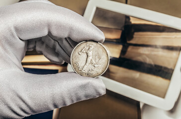 Photo of a person's male hand in white gloves holding a soviet silver 1924 half ruble coin on stack...