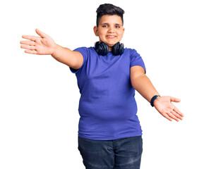 Little boy kid listening to music wearing headphones looking at the camera smiling with open arms for hug. cheerful expression embracing happiness.