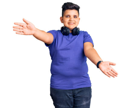 Little boy kid listening to music wearing headphones looking at the camera smiling with open arms for hug. cheerful expression embracing happiness.