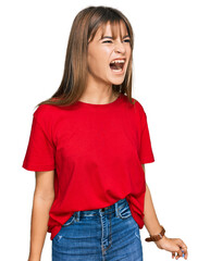 Obraz premium Teenager caucasian girl wearing casual red t shirt angry and mad screaming frustrated and furious, shouting with anger. rage and aggressive concept.