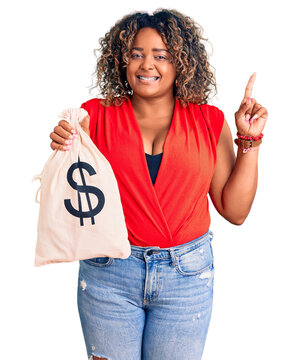 Young african american plus size woman holding money bag with dollar symbol surprised with an idea or question pointing finger with happy face, number one
