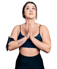 Young hispanic woman wearing sportswear begging and praying with hands together with hope...