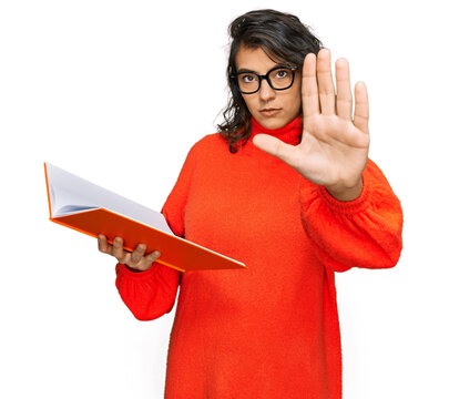 Young hispanic woman reading a book wearing glasses with open hand doing stop sign with serious and confident expression, defense gesture