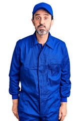 Middle age handsome man wearing mechanic uniform puffing cheeks with funny face. mouth inflated with air, crazy expression.