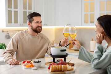 Fototapeta na wymiar Romantic date with fondue. Couple clinking glasses of wine at home