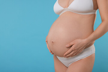 Fototapeta na wymiar Pregnant woman in stylish comfortable underwear on light blue background, closeup. Space for text