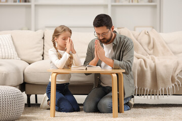 Girl and her godparent praying over Bible together at table indoors - obrazy, fototapety, plakaty
