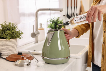 Woman pouring vinegar from bottle into electric kettle in kitchen, closeup