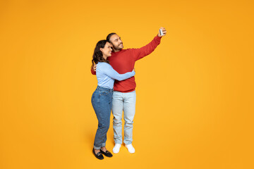 Fototapeta na wymiar Loving millennial couple embracing and taking selfie on phone