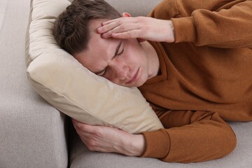 Sad man suffering from headache on sofa indoors