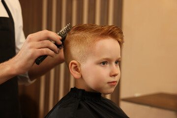 Professional hairdresser brushing boy's hair in beauty salon, closeup