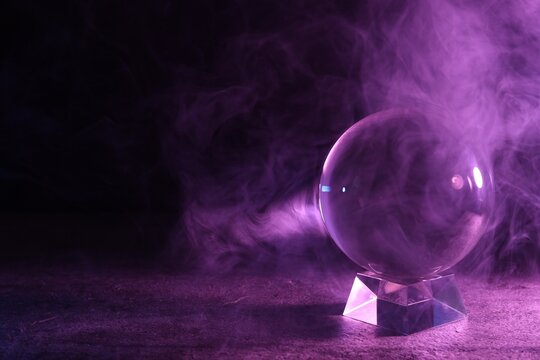 Crystal ball on table and smoke against dark background, space for text. Predictions of future