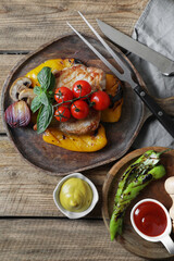 Delicious grilled meat and vegetables served with sauces on wooden table, flat lay