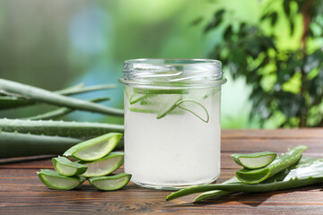 Fresh aloe juice in jar and leaves on wooden table outdoors, closeup