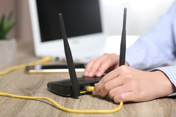 Woman inserting ethernet cable into Wi-Fi router at wooden table indoors, closeup