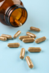Bottle and vitamin capsules on light blue background, closeup