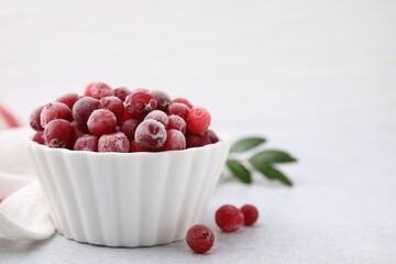 Frozen red cranberries in bowl on light table, closeup. Space for text