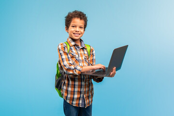 Smiling boy with laptop and backpack ready for school