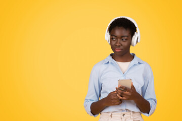 Focused teen african american lady student in wireless headphones, listen music, use phone