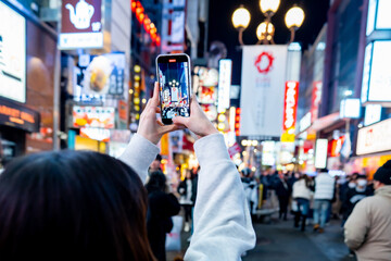 female tourist taking a photo with the famous night shopping street food at Dotonbori or dotombori, Dotonbori the famous destination for traveller in Shinsaibashi, Osaka City, Osaka, Japan.