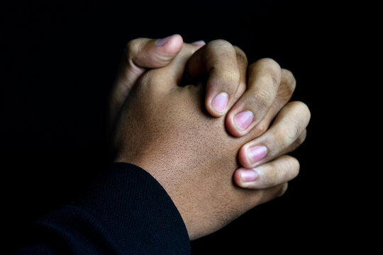 close up of man praying hands on dark background