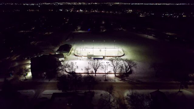 Canadian winter night scene, outdoor hockey rinks illuminated by floodlight and city skyline, 4K drone shot