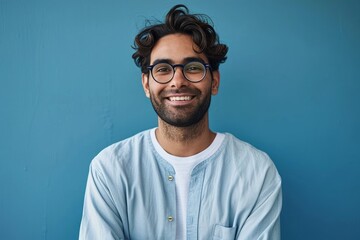 Smiling confident arab young man, male student, professional employee or programmer standing isolated on blue background. Happy handsome ethnic guy wearing shirt and glasses, Generative AI  - obrazy, fototapety, plakaty