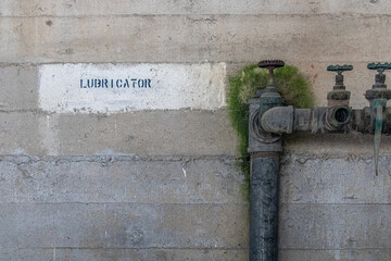 Lubricator. Decal painting on concrete wall of an abandoned airplane hanger. Rusted old pipes remain next to the spot for old equipment. Textured and moody industrial space