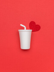 A large white drink glass with a straw and a red heart on a red background.
