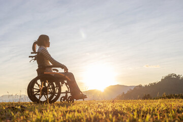 Silhouette Girl in wheelchair looking sunset mountain background.