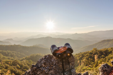 binoculars on top of rock mountain at beautiful sunset background.