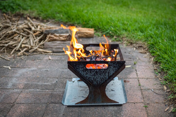 Campfire, fire pit filled with burnt wood and flames. Chopped fire wood in background.