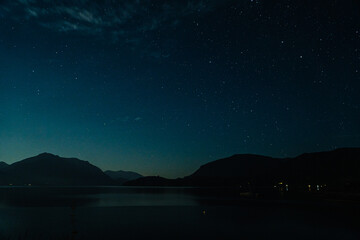 Village by the lake under a starlit blue sky with the mesmerizing presence of the Milky Way. - obrazy, fototapety, plakaty